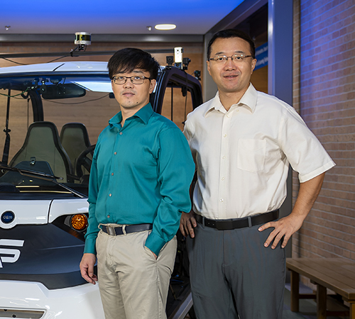 Qing Yang and Song Fu stand to the right of a connected and autonomous golf cart