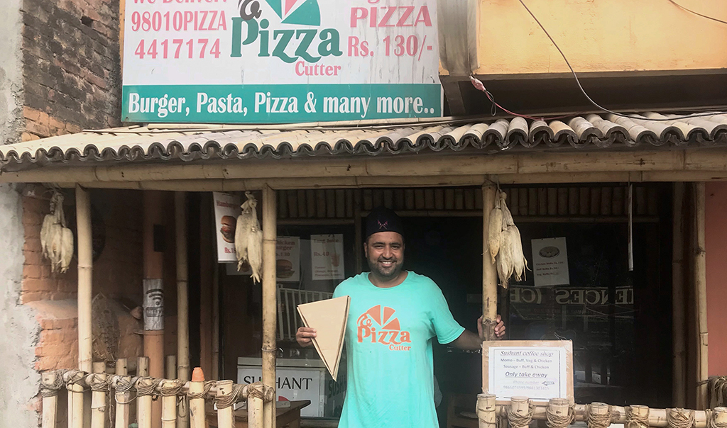Prasanna Aryal stands in front of The Pizza Cutter holding a pizza shaped box