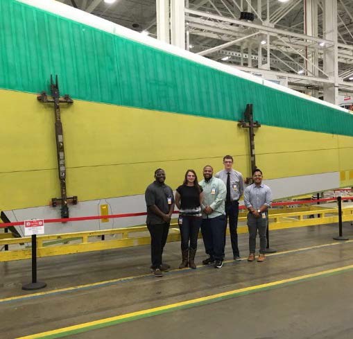 Team members in front of a huge aircraft skin panel