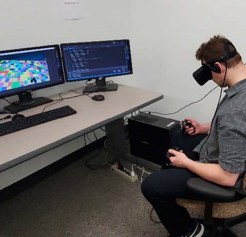 A student wearing Vitual Reality goggle in front of two computer screens showing the visualiztion