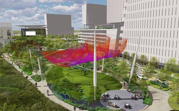 The park with trees, green grass, a sitting area and a red sun screen sail