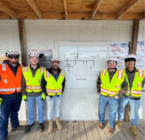 Team members pose on the site with drawings on the wall
