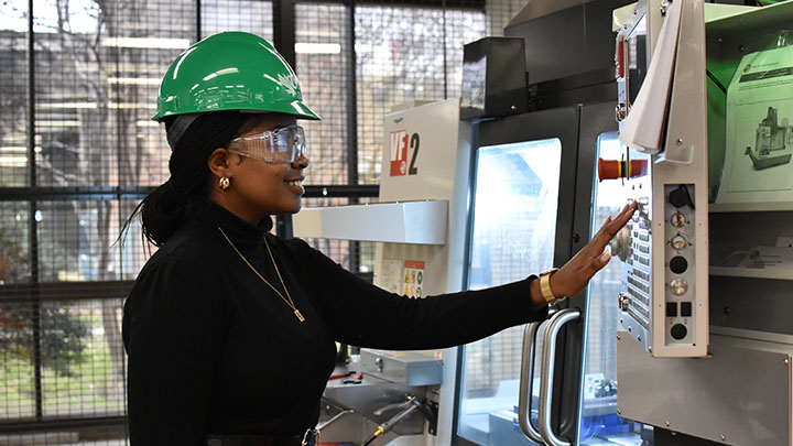 A female student wearing safety helmet and glasses operating lab equipment