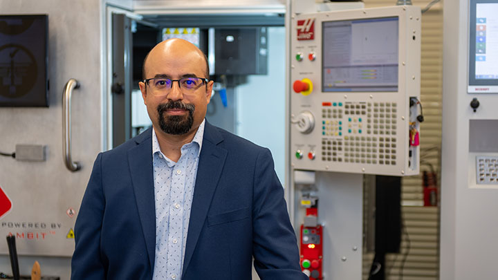 Faculty member poses in lab in front of equipment