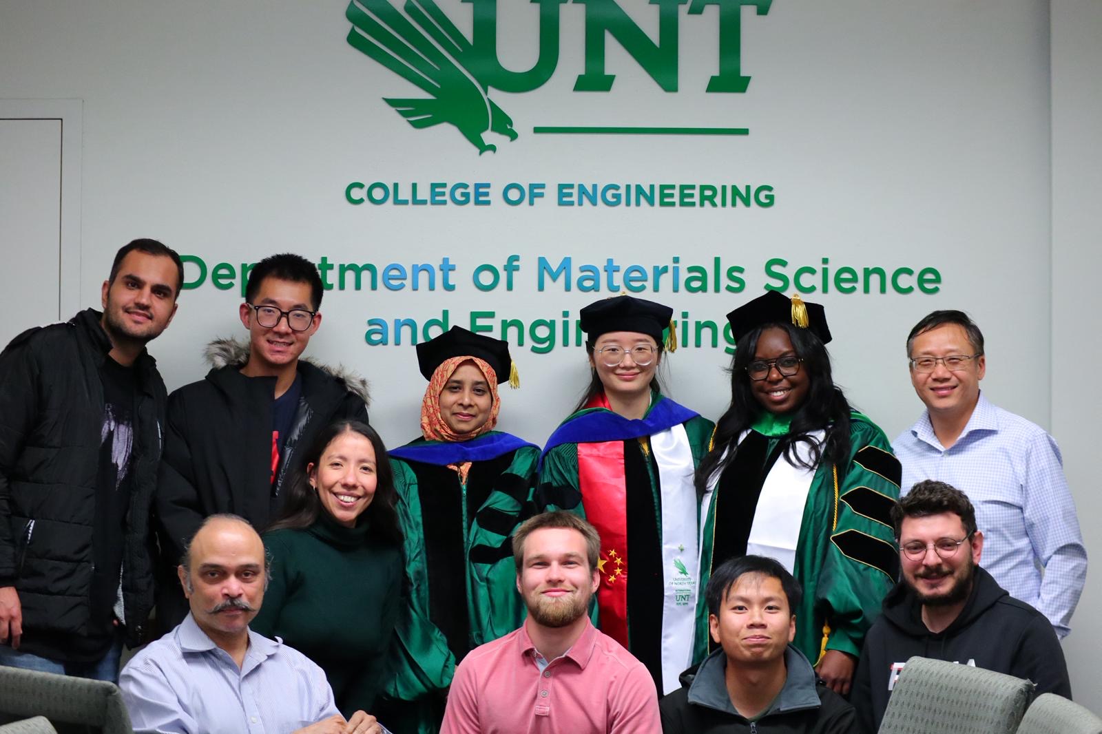 Dr. Du and students pose in front of a backdrop of UNT Materials Science and Engineering