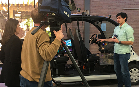 PhD student shows nearly autonomous vehicle to cameraman. 