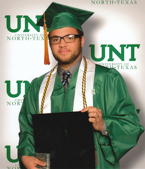 Jacob Montgomery Cole stands in a UNT graduation cap and gown, posing with his diploma frame in fron