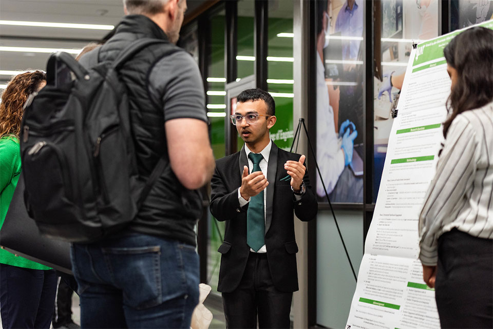 A student standing in front of a research poster explaining his work to others