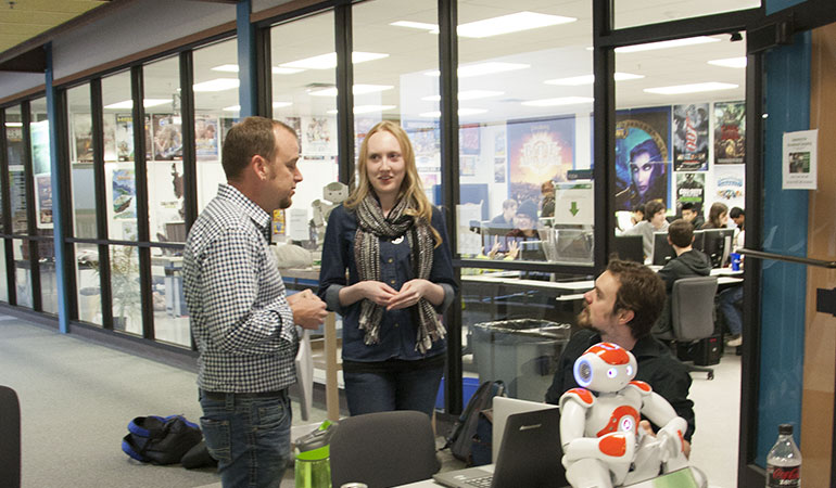 Two graduate students talking with a faculty in front of game programming lab