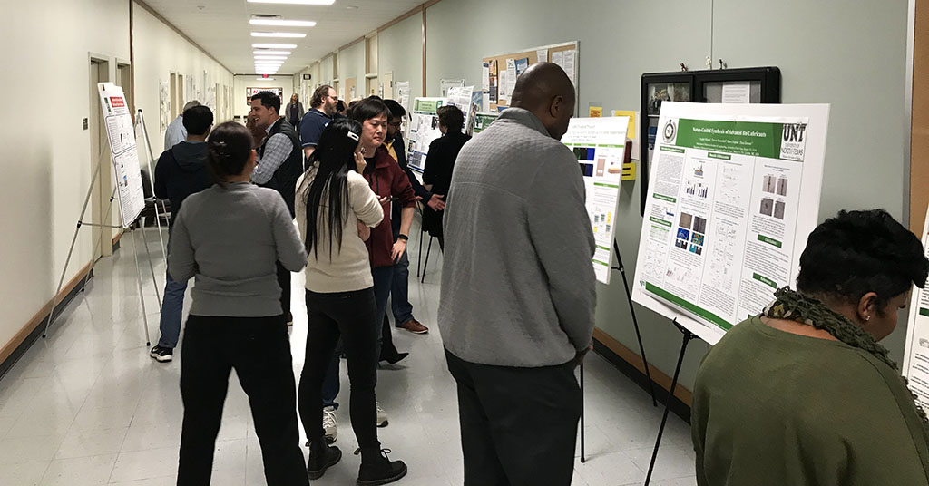 Students present posters to fellow students, their faculty, and judges in a hallway.