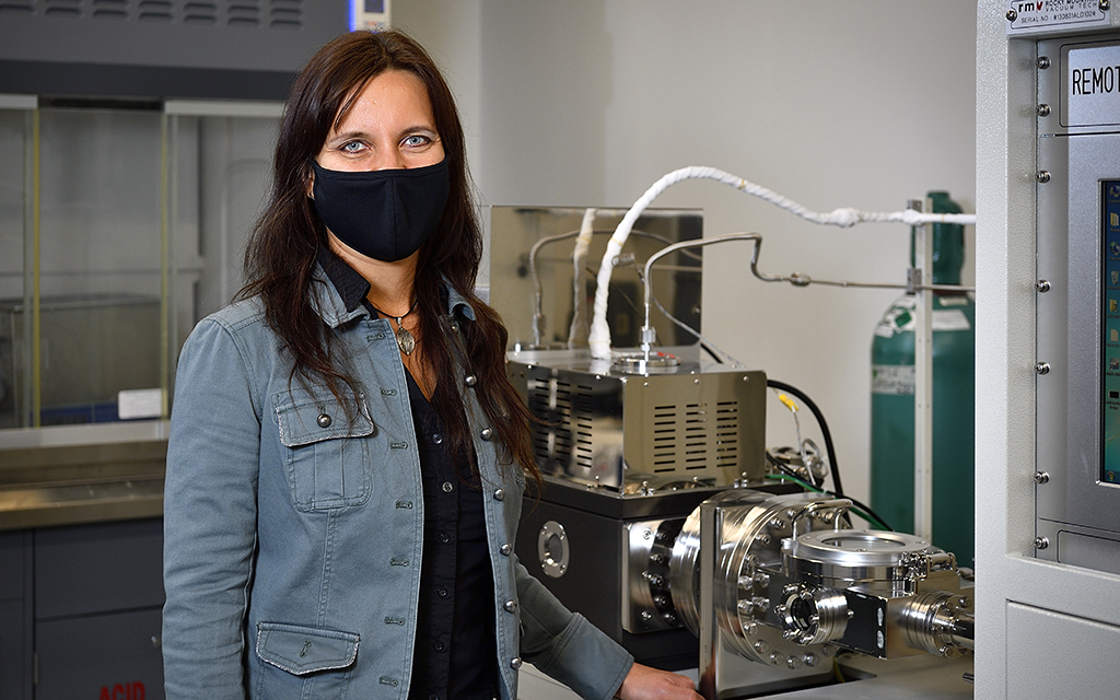 Diana Berman stands in front of machinery in a materials science lab