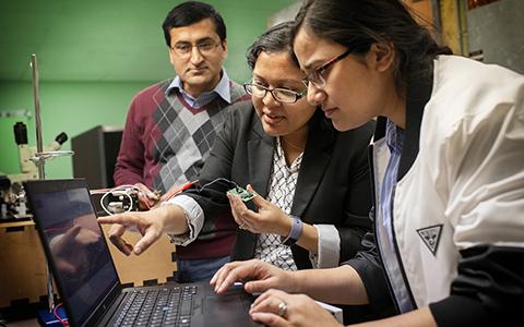 Ifana Mahbub and two graduate students lean over a laptop while holding a chip