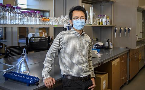 Clement Chan stands in the lab in front of a counter with vials