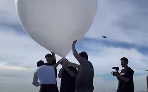 Four people hold on to the weather balloon while one person videos the balloon launch.