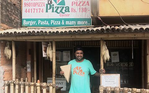 Prasanna Aryal stands in front of The Pizza Cutter holding a pizza shaped box